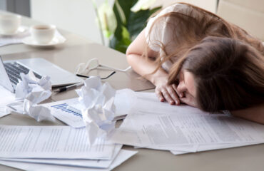 Woman sleeping on desk covered crumpled papers